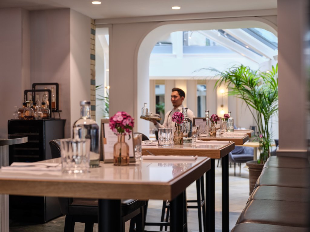 Restaurantbereich mit gedeckten Holztischen, Blumen und Blick in den hellen Innenraum der UNA Tagesbar